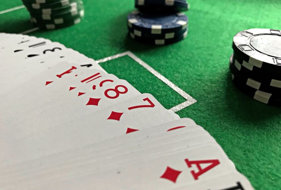 Setumpuk kartu remi dan chip poker di atas meja felt hijau